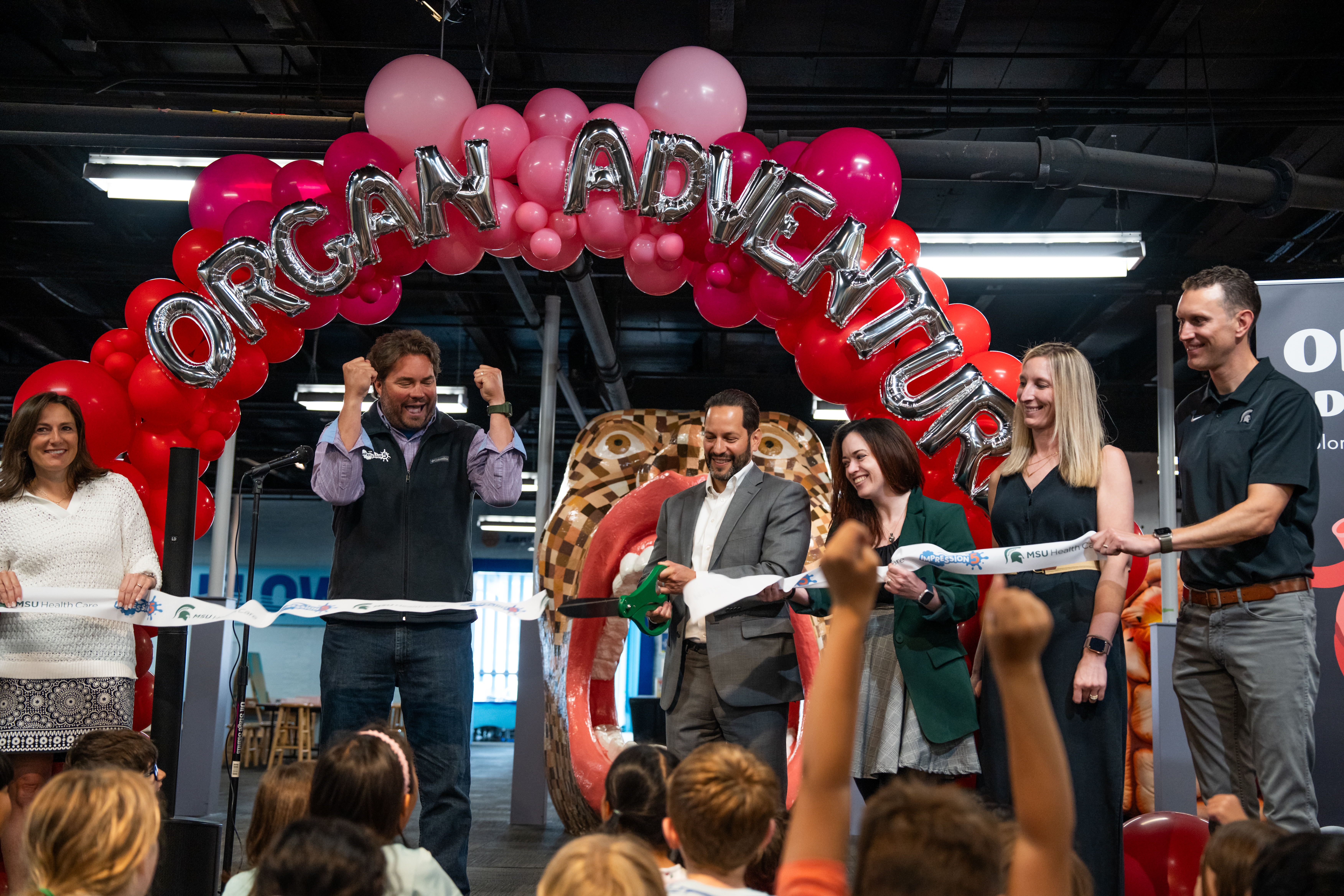 a group of people cutting a ribbon at science center exhibit opening